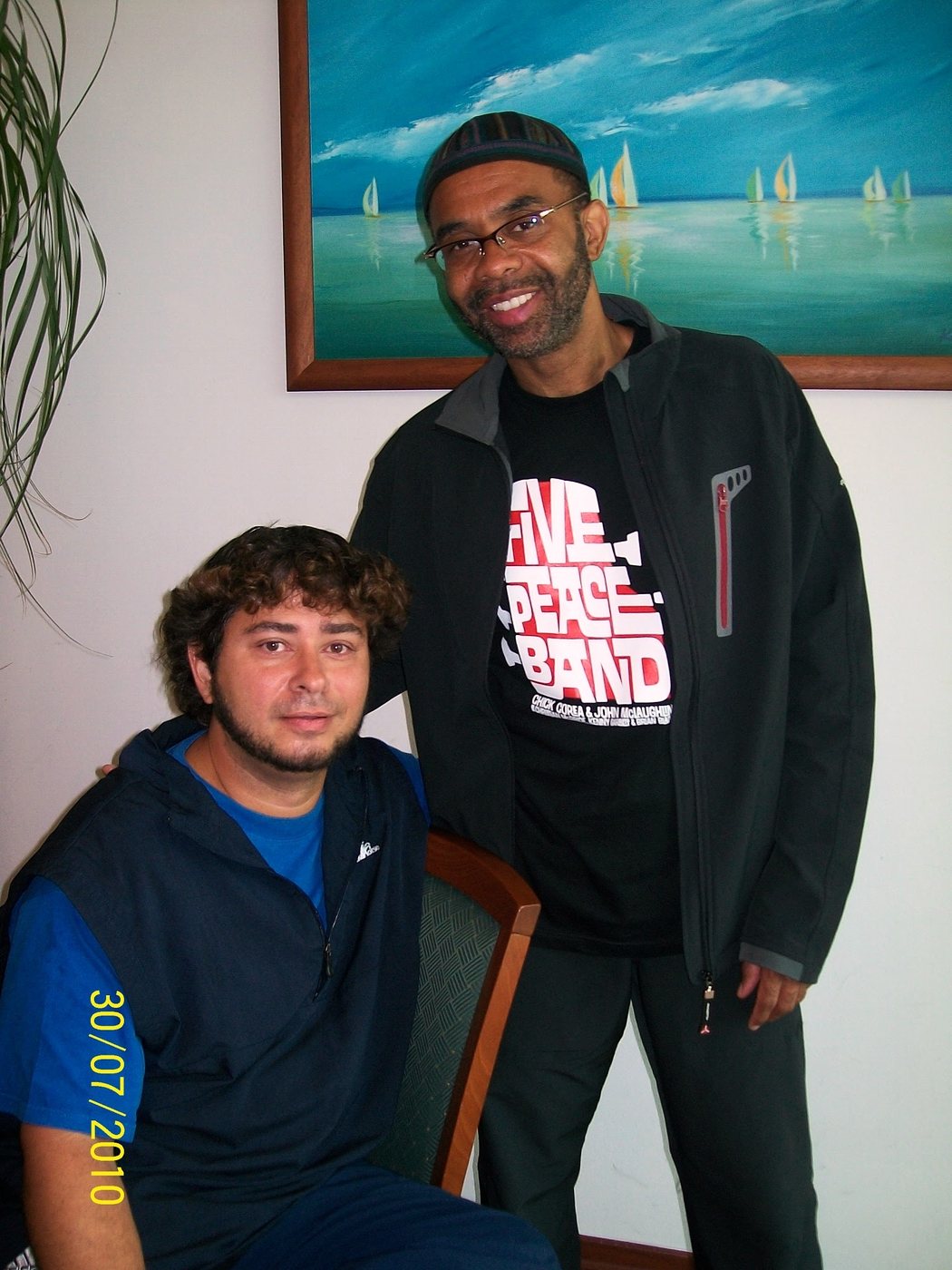 Yan Kayary sentado junto a Kenny Garrett, de pie, frente a un cuadro de veleros
