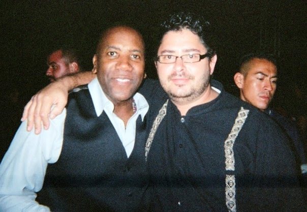 Yan Kayary abrazado por un hombre de chaleco oscuro sobre camisa clara