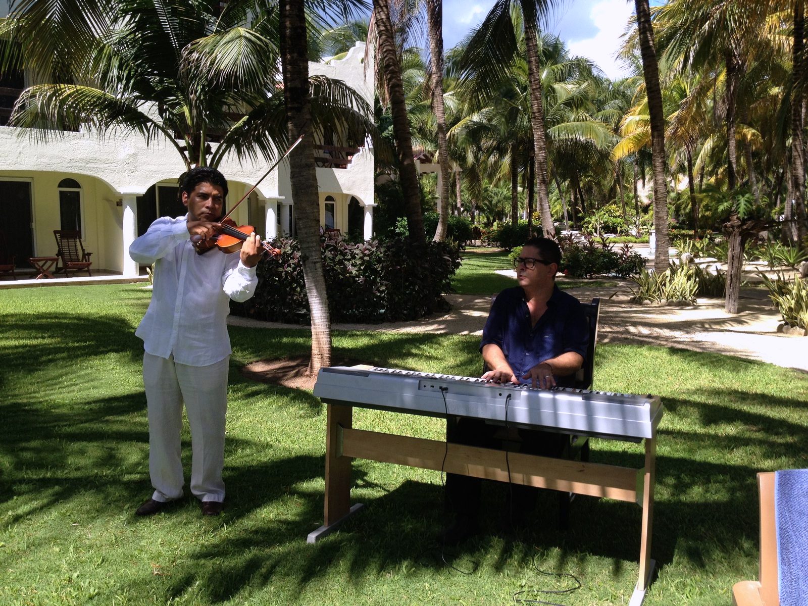 Yan al teclado acompañando a un violinista en un jardín
