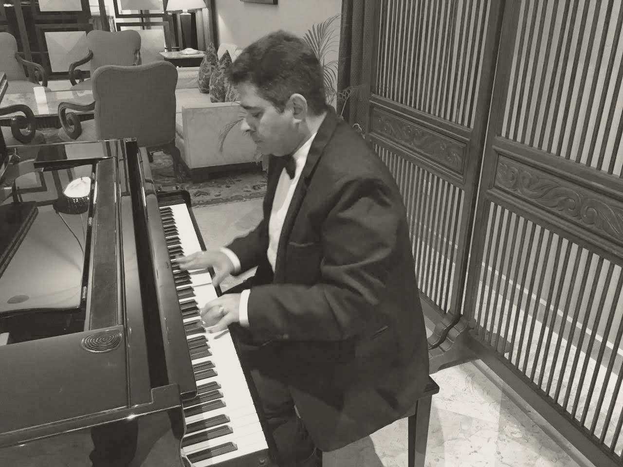 Yan Kayary de traje negro y moño, tocando un piano de cola junto a un biombo de madera